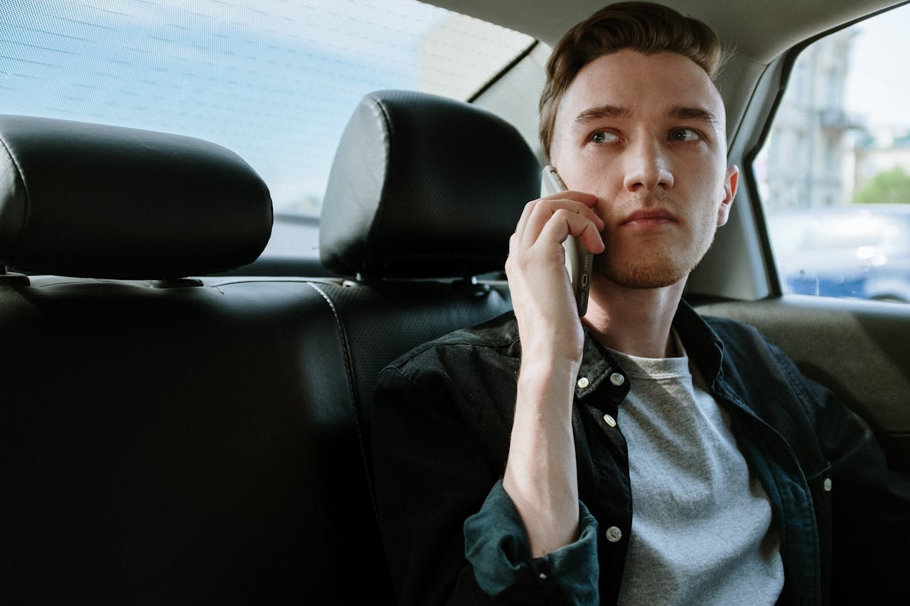 A young man talking on his phone while sitting in the backseat of a car.