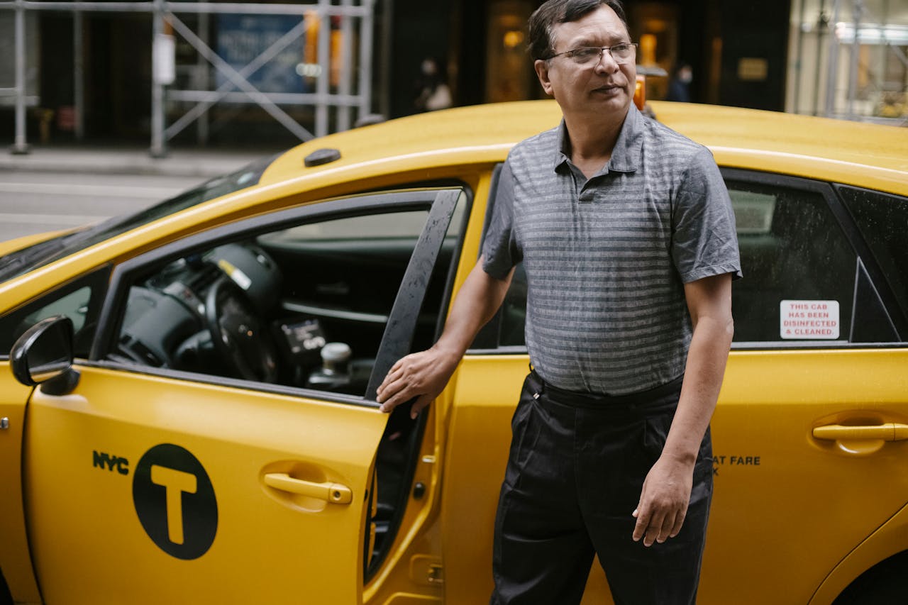 Middle-aged male taxi driver standing by yellow cab in New York City street.